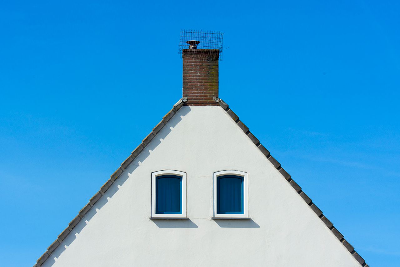 A minimalist house facade with a chimney against a bright blue sky, showcasing symmetry and simplicity.